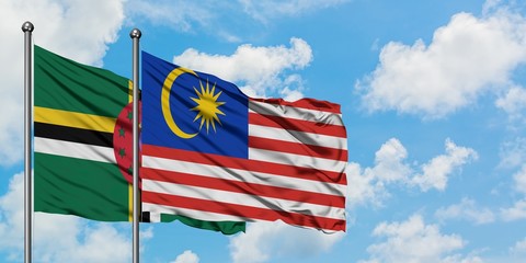 Dominica and Malaysia flag waving in the wind against white cloudy blue sky together. Diplomacy...