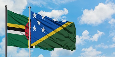 Dominica and Solomon Islands flag waving in the wind against white cloudy blue sky together....