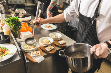 Professional chef cooking in the kitchen restaurant at the hotel, preparing dinner. A cook in an apron makes a salad of vegetables and pizza.