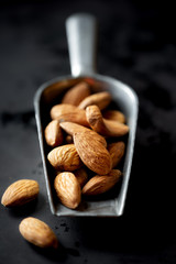Almonds in a vintage measuring scoop against black background. Shallow depth of field
