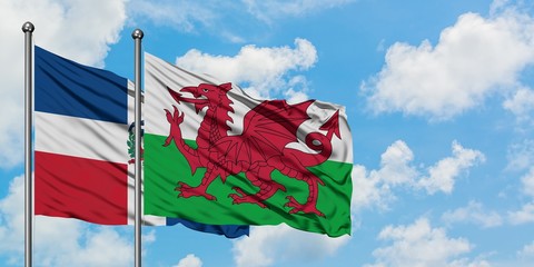Dominican Republic and Wales flag waving in the wind against white cloudy blue sky together....