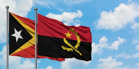 East Timor and Angola flag waving in the wind against white cloudy blue sky together. Diplomacy concept, international relations.