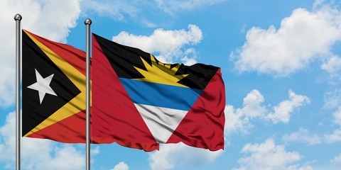 East Timor and Antigua and Barbuda flag waving in the wind against white cloudy blue sky together....