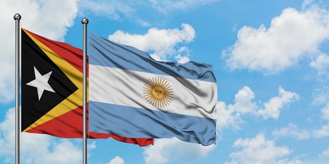 East Timor and Argentina flag waving in the wind against white cloudy blue sky together. Diplomacy...