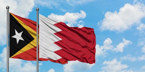 East Timor and Bahrain flag waving in the wind against white cloudy blue sky together. Diplomacy...