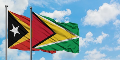 East Timor and Guyana flag waving in the wind against white cloudy blue sky together. Diplomacy concept, international relations.