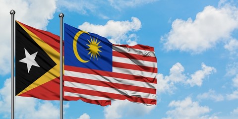 East Timor and Malaysia flag waving in the wind against white cloudy blue sky together. Diplomacy concept, international relations.