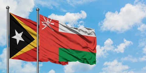 East Timor and Oman flag waving in the wind against white cloudy blue sky together. Diplomacy concept, international relations.