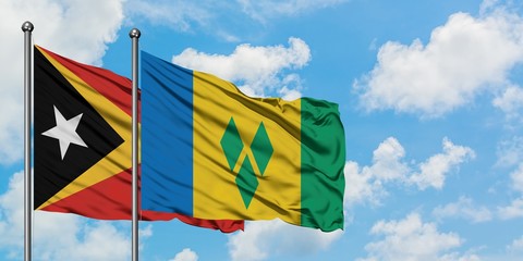 East Timor and Saint Vincent And The Grenadines flag waving in the wind against white cloudy blue sky together. Diplomacy concept, international relations.