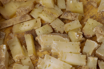 Hard cheese is cut into small pieces. French traditional cheese on a wooden background.