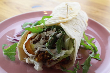 Delicious beef burrito with salad and cheese on a white plate.