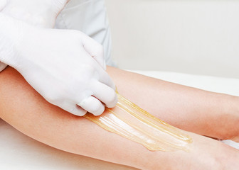 Cosmetologist beautician waxing female legs in the spa center beauty salon closeup