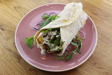 Delicious beef burrito with salad and cheese on a white plate.
