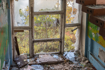 View on nature landscape thru the broken window of ruined abandoned building. Glass shatters on the floor. Maybe post apocalypse ore something