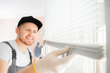 Worker in uniform installing blinds on plastic upvc window