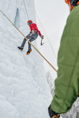 Alpinist woman with ice tools axe in orange helmet climbing a l