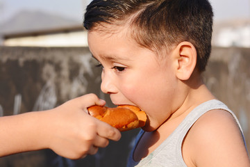 Little latin boy eating bread outside.