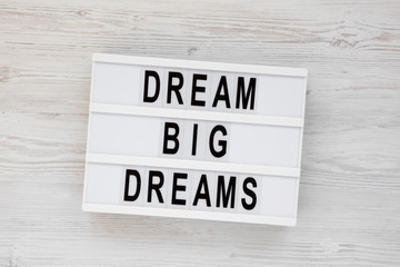 'Dream big dreams' words on a lightbox on a white wooden background, top view. Overhead, from above, flat lay.
