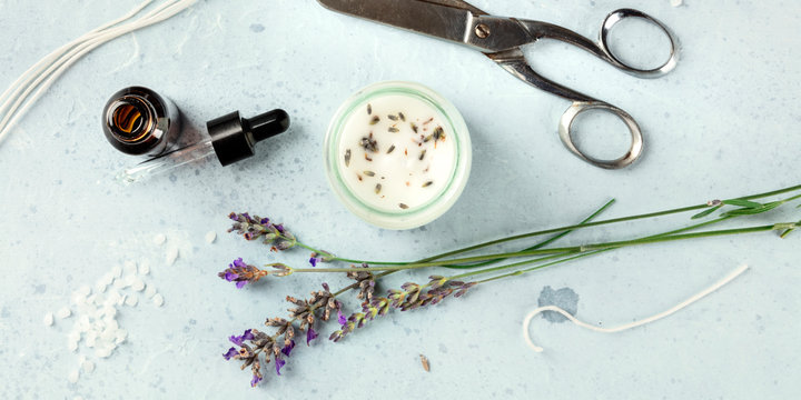 Handmade lavender scented candle with essential oil, flowers, wax, wicks, and scissors, overhead panoramic flat lay shot. An artisanal Christmas gift in a recycled glass jar