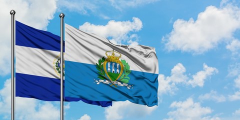 El Salvador and San Marino flag waving in the wind against white cloudy blue sky together. Diplomacy concept, international relations.