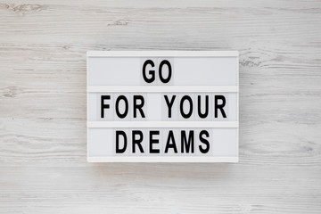 'Go for your dreams' words on a lightbox on a white wooden surface, top view. Overhead, from above, flat lay.