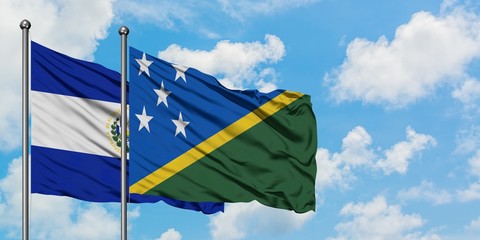 El Salvador and Solomon Islands flag waving in the wind against white cloudy blue sky together. Diplomacy concept, international relations.