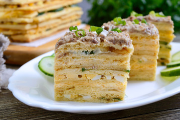 Layer cake with eggs, cheese, green onions, canned fish, mayonnaise on a white plate on a wooden table. Festive appetizer. Close-up.
