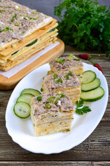 Layer cake with eggs, cheese, green onions, canned fish, mayonnaise on a white plate on a wooden table. Festive appetizer.