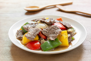 close up of stir fried beef with black and sweet pepper in a ceramic dish on wooden table. homemade style food concept.