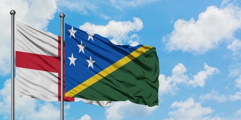 England and Solomon Islands flag waving in the wind against white cloudy blue sky together....