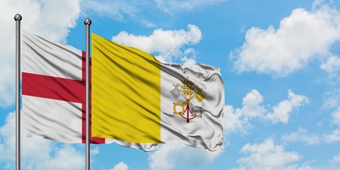 England and Vatican City flag waving in the wind against white cloudy blue sky together. Diplomacy concept, international relations.
