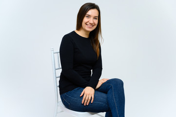 Portrait of an adult woman without makeup with clean skin, with long brown hair over her face on a white background. Sits on a chair in a black T-shirt, shows with his hands emotions.