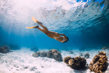 Girl freediver glides with yellow fins over sandy sea.