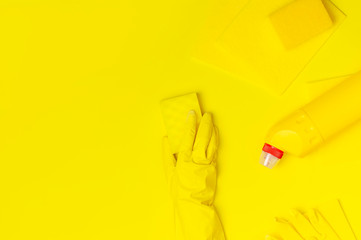 House cleaning concept. Women's hands in yellow rubber gloves, household chemicals, bleach, antibacterial gel, sponge, rags on yellow background. Flat lay top view copy space. Cleaning accessories