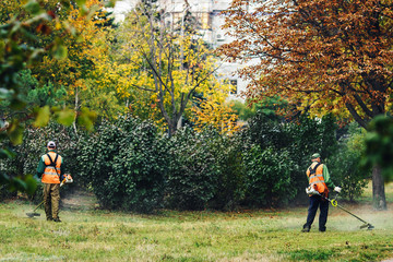 Two men in a park mowing grass with mowers.
