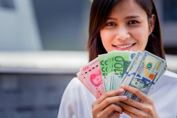 Happiness businesswoman holding USD dollars, yuan RMB, Euro money choosing and thinking for business investment.