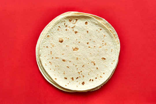 Tortillas on red background. A pile of  baked blank corn tortilla wraps on a color background with copy space. Top view or flat lay for use as a cooking, mexican restaurant or travel background.