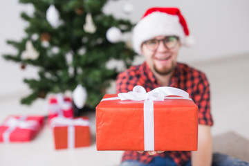 Christmas and holidays concept - Funny man in santa hat holding a gift at home in the living room