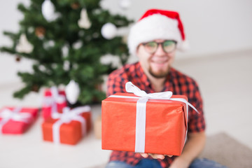 Christmas and holidays concept - Funny man in santa hat holding a gift at home in the living room