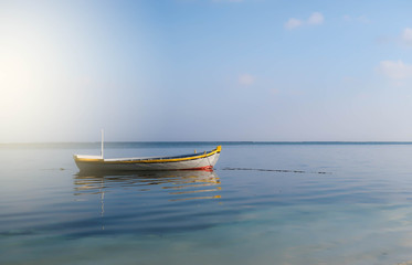 Fototapeta premium A small boat is responsible for serving tourist or lover to do marine activities. It's not yet installed the engine parked at the beach on the day with clear sky, calm waves, Maafushi Island, Maldives