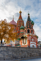 Saint Basil Cathedral on Red square in sunny autumn evening. View on a background of blue sky with clouds and autumn tree with golden leaves