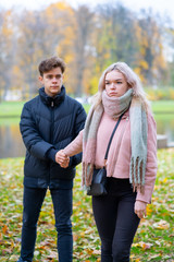 Fototapeta premium Two teenagers in love in quarrel. The blonde girl takes offense at boy, the guy holds her hand, asks the girl to stay and not leave. Concept of difficulties in adolescent relationships