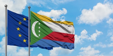 European Union and Comoros flag waving in the wind against white cloudy blue sky together....