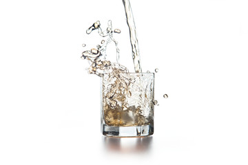 Whiskey pouring into glass with ice on light background..