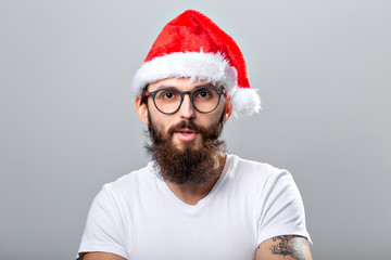 Holidays and people concept - Portrait of a handsome brutal man in Christmas hat. Over grey background.
