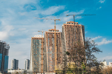 Fototapeta na wymiar Construction of high-rise buildings in the city with tower crane with lifting boom in daytime