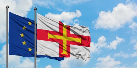 European Union and Guernsey flag waving in the wind against white cloudy blue sky together. Diplomacy concept, international relations.