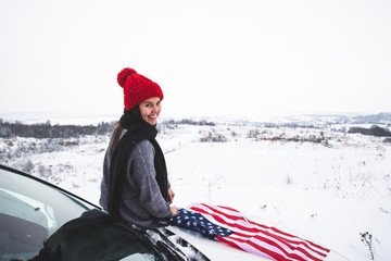 young adult woman traveler sitting on the hood of the suv car with usa flag
