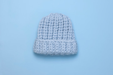 Flat lay fashionable blue knitted winter hat for women on blue background top view. Stylish woolen hat, concept of winter accessories for the cold. Advertising, shopping, winter sale