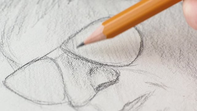 Sketch in a notebook: hand with a pencil draws a man’s face in glasses. The concept of sketching, teaching drawing.